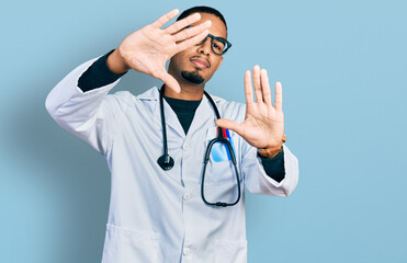 Young african american man wearing doctor uniform and stethoscope doing frame using hands palms and fingers, camera perspective