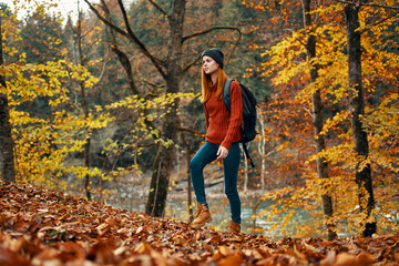 woman tourist walks through the park in autumn with a backpack on her back and tall trees landscape river lake