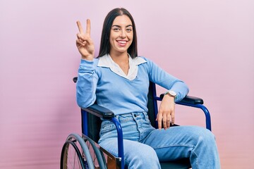 Beautiful woman with blue eyes sitting on wheelchair showing and pointing up with fingers number...