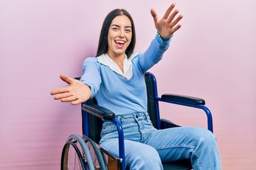 Beautiful woman with blue eyes sitting on wheelchair looking at the camera smiling with open arms...