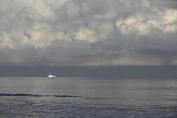 A white ship in the sea on the horizon. An image of an ocean liner on silvery water with lush gray clouds in the morning mist.Photo of a monochrome seascape