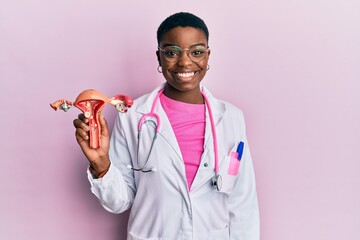 Young african american doctor woman holding anatomical model of female genital organ looking...