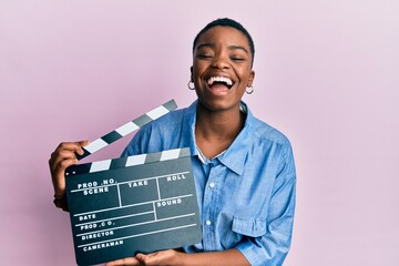 Young african american woman holding video film clapboard smiling and laughing hard out loud because funny crazy joke. - obrazy, fototapety, plakaty