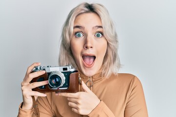 Young blonde girl holding vintage camera celebrating crazy and amazed for success with open eyes screaming excited.