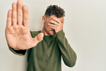 Fototapeta premium Young hispanic man wearing casual clothes covering eyes with hands and doing stop gesture with sad and fear expression. embarrassed and negative concept.