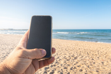 Close-up of a Caucasian man's hand using a smartphone on the beach.