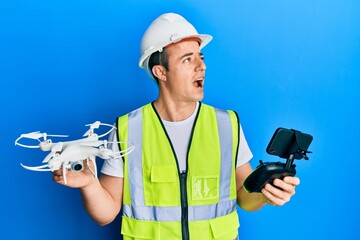 Handsome young man wearing safety hard using drone and control angry and mad screaming frustrated and furious, shouting with anger looking up.