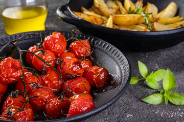 plate of confit tomatoes  and roasted potatoes with rosemary in iron casserole on dark background