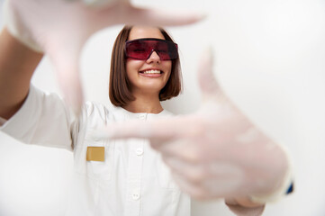 Happy female doctor smiling with toothy smile while looking through her fingers frame