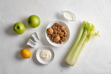 Ingredients for making a Waldorf salad made of celery, apples and walnuts on a light concrete background