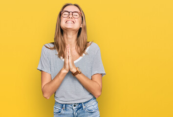 Beautiful young blonde woman wearing casual clothes and glasses begging and praying with hands...