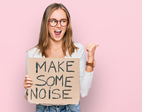 Beautiful blonde woman holding make some noise banner pointing thumb up to the side smiling happy with open mouth