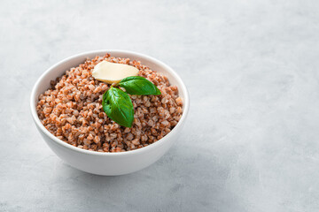 Boiled buckwheat with basil and butter on a gray background. Side view, copy space.