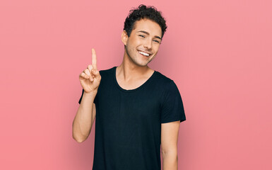 Young handsome man wearing casual black t shirt showing and pointing up with finger number one while smiling confident and happy.