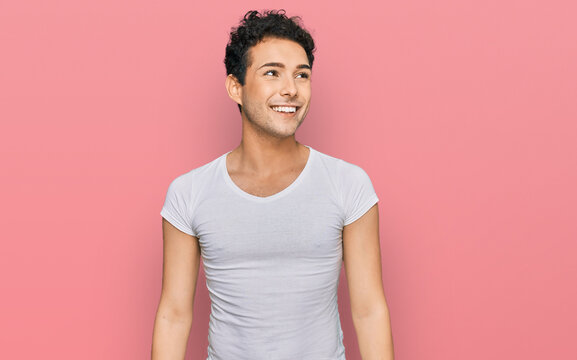 Young handsome man wearing casual white t shirt looking away to side with smile on face, natural expression. laughing confident.
