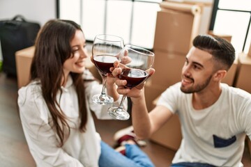 Young hispanic couple smiling happy toasting with red wine at new home.