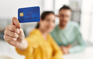 Young hispanic couple holding credit card at home.