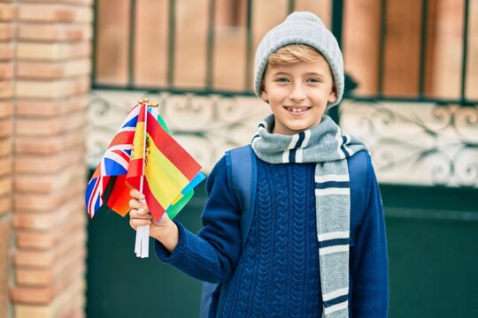 Adorable blond student kid smiling happy holding flags of different countries at the school.