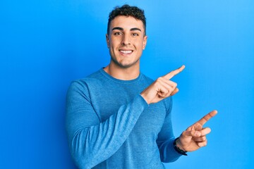 Hispanic young man wearing casual winter sweater smiling and looking at the camera pointing with two hands and fingers to the side.