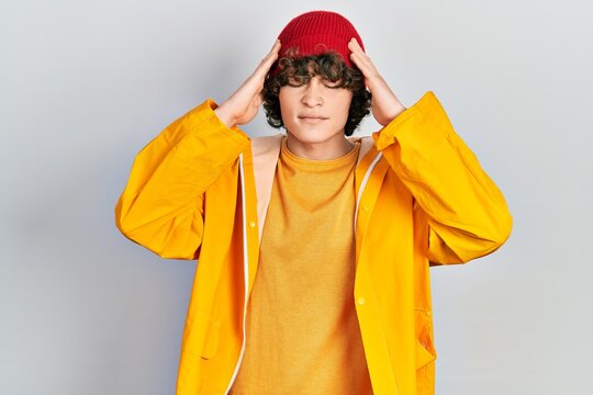 Handsome young man wearing yellow raincoat suffering from headache desperate and stressed because pain and migraine. hands on head.