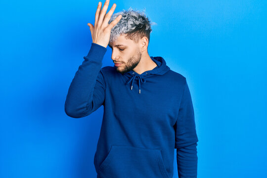 Young hispanic man with modern dyed hair wearing casual blue sweatshirt surprised with hand on head for mistake, remember error. forgot, bad memory concept.