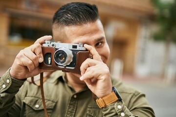 Young latin tourist man smiling happy using vintage camera at the city.