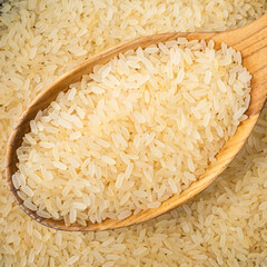 raw parboiled rice in wooden spoon closeup