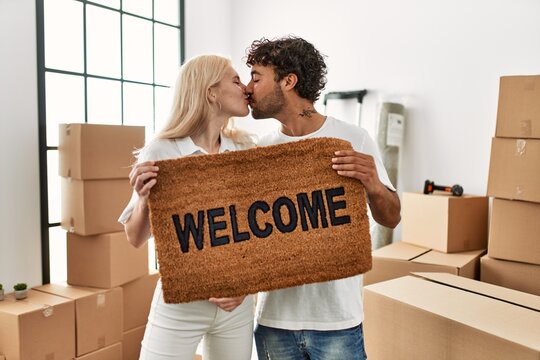 Young beautiful couple smiling happy holding welcome doormat at new home.