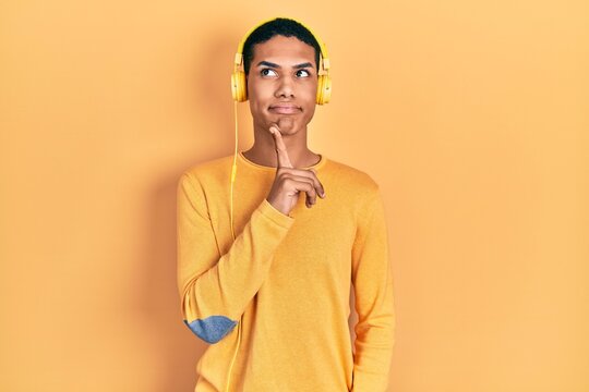 Young african american guy listening to music using headphones thinking concentrated about doubt with finger on chin and looking up wondering