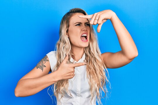 Beautiful young blonde woman doing picture frame gesture with hands angry and mad screaming frustrated and furious, shouting with anger. rage and aggressive concept.