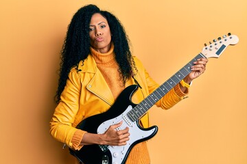 Middle age african american woman playing electric guitar looking at the camera blowing a kiss being lovely and sexy. love expression.