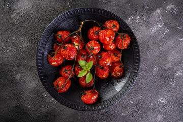Black plate with confit tomatoes on dark background