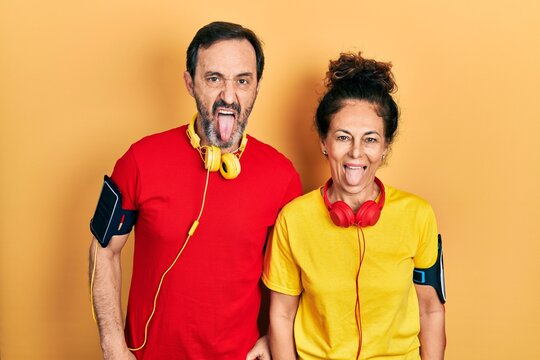 Middle age couple of hispanic woman and man wearing sportswear and arm band sticking tongue out happy with funny expression. emotion concept.