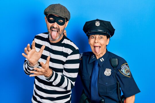 Middle age couple of hispanic woman and man wearing thief and police uniform sticking tongue out happy with funny expression. emotion concept.