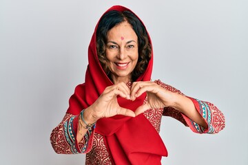 Middle age hispanic woman wearing tradition sherwani saree clothes smiling in love doing heart...
