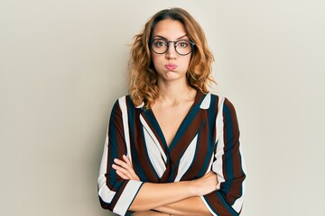 Young caucasian woman wearing business shirt and glasses puffing cheeks with funny face. mouth inflated with air, catching air. - obrazy, fototapety, plakaty