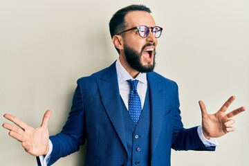 Young man with beard wearing business suit and tie crazy and mad shouting and yelling with aggressive expression and arms raised. frustration concept.