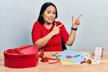 Beautiful hispanic woman with nose piercing doing handcraft creative decoration pointing aside...