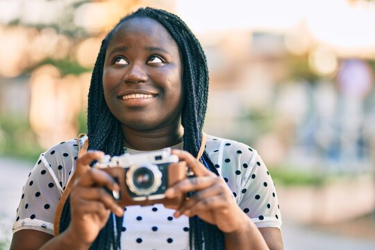 Young african american tourist woman smiling happy using vintage camera at the city.