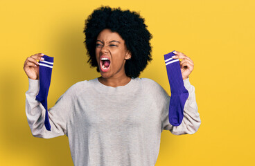 Young african american woman holding socks angry and mad screaming frustrated and furious, shouting...