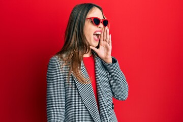 Young brunette woman wearing fashion and modern look shouting and screaming loud to side with hand on mouth. communication concept.