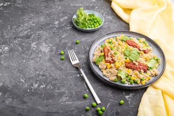 Quinoa porridge with green pea, corn and dried tomatoes on ceramic plate on a gray concrete background. Side view, copy space.