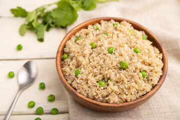 Quinoa porridge with green pea in wooden bowl on a white wooden background. Side view, selective focus.