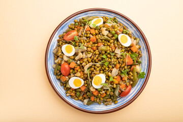 Mung bean porridge with quail eggs, tomatoes and microgreen sprouts on a pastel orange background. Top view.