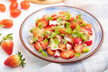 Vegetarian fruits and vegetables salad of strawberry, kiwi, tomatoes, microgreen sprouts on white concrete background. Side view, selective focus.