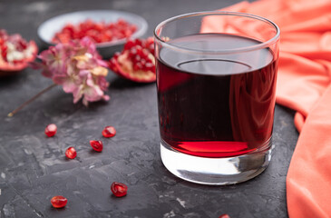 Glass of pomegranate juice on a black concrete background. Side view, selective focus.