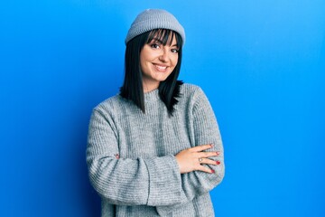 Young hispanic woman wearing wool sweater and winter hat happy face smiling with crossed arms...