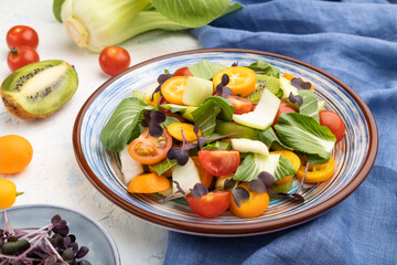 Vegetarian salad of pac choi cabbage, kiwi, tomatoes, kumquat, microgreen sprouts on a white concrete background. Side view.