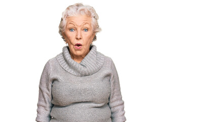 Senior grey-haired woman wearing casual winter sweater in shock face, looking skeptical and...