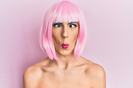 Young man wearing woman make up wearing pink wig making fish face with lips, crazy and comical gesture. funny expression.